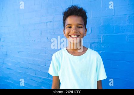 Ein birassischer Junge lächelt hell gegen eine blaue Wand Stockfoto