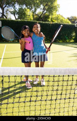 Draußen lächeln zwei junge Schwestern auf dem Tennisplatz und halten Tennisschläger Stockfoto