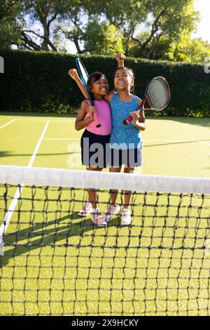 Zwei junge Schwestern, die lächeln, halten Tennisschläger draußen auf einem Tennisplatz Stockfoto