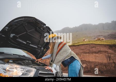 Eine Frau mit gelbem Hut steht neben einem Auto mit aufgesetzter Kapuze, Touristen in den peruanischen anden. Stockfoto