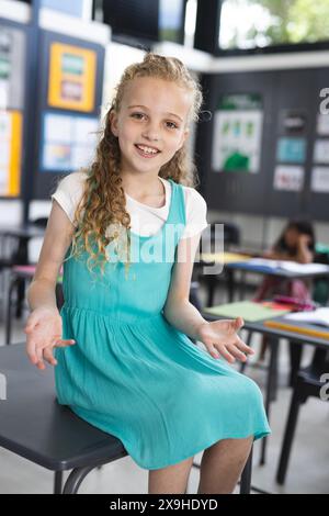 Ein weißes Mädchen mit lockigen blonden Haaren trägt ein blaues Kleid in einer Schulklasse Stockfoto