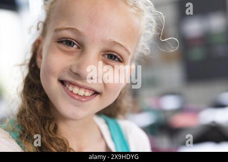 Kaukasisches Mädchen, lockiges blondes Haar, Lächeln mit Sommersprossen im Klassenzimmer Stockfoto