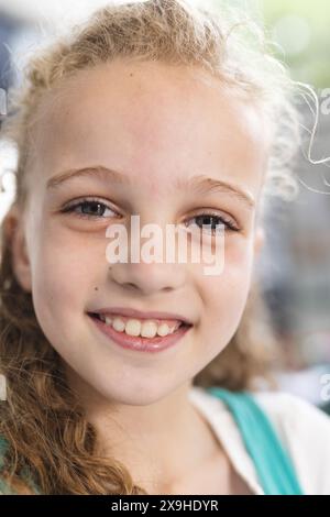 Ein weißes Mädchen mit lockigen Haaren lächelt in einem Schulzimmer warm und zeigt ihre Sommersprossen Stockfoto