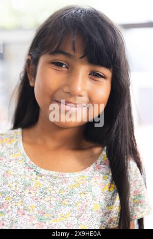 Ein birassisches Mädchen mit einem warmen Lächeln, das ein Blumenkleid in einer Schulklasse trägt Stockfoto