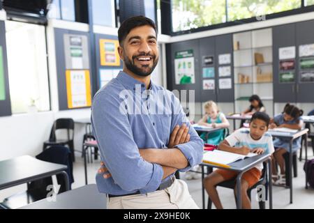 In der Schule steht ein asiatischer Lehrer lächelnd mit überkreuzten Armen im Klassenzimmer Stockfoto