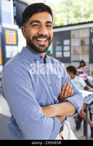 Junger asiatischer Lehrer mit Bart lächelt selbstbewusst in einem Schulzimmer Stockfoto