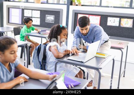 Ein junger asiatischer Lehrer führt ein birassisches Mädchen an einen Laptop Stockfoto