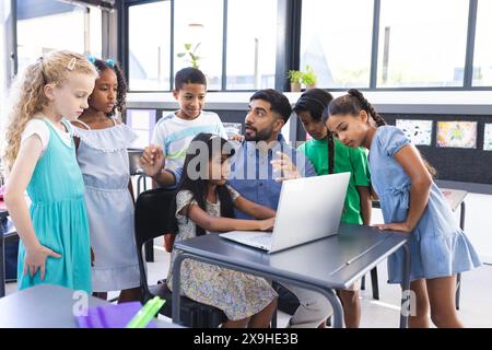 In der Schule schauen junge asiatische Lehrer und verschiedene Schüler im Klassenzimmer auf einen Laptop Stockfoto