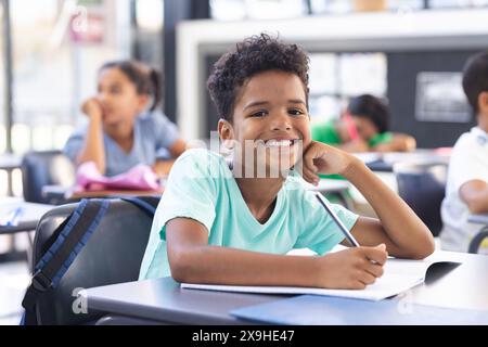 In der Schule schreibt ein junger, birassischer Junge mit lockigen Haaren im Klassenzimmer Stockfoto