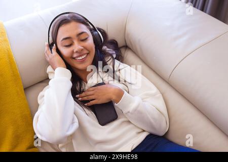 Eine birassische junge Frau, die Kopfhörer trägt und sich zu Hause entspannt Stockfoto