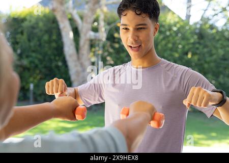 Im Freien, männlicher Physiotherapeut und ältere Patientin mit Kurzhanteln. Sie befinden sich im sonnigen Garten und konzentrieren sich auf Kraft- und Mobilitätstraining Stockfoto