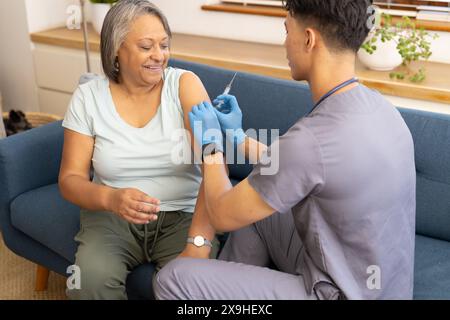 Zu Hause, junge männliche Krankenschwester, die eine ältere Patientin erschossen. Sie befinden sich in einem gemütlichen Wohnzimmer mit blauem Hintergrund, einem blauen Sofa und einem Windo Stockfoto