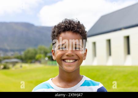 Ein birassischer Junge mit lockigen Haaren lächelt draußen und trägt ein gestreiftes Hemd Stockfoto