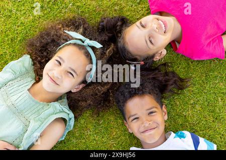 Drei Kinder liegen auf dem Gras und lächeln in die Kamera Stockfoto