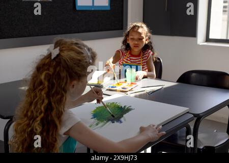 Kaukasische und birassische Mädchen malen in einem sonnendurchfluteten Zimmer in der Schule Stockfoto