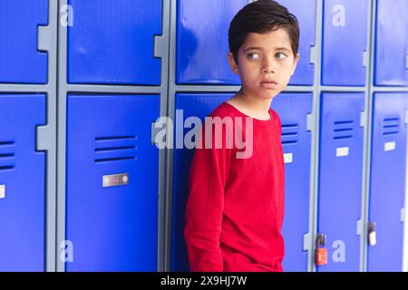 In der Schule lehnte sich ein junger männlicher Schüler gegen blaue Schließfächer im Freien Stockfoto