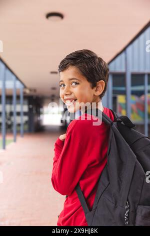 In der Schule lächelt ein junger männlicher Student mit rotem Hemd draußen Stockfoto