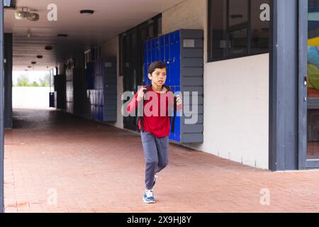 In der Schule läuft ein junger männlicher Student mit rotem Hemd draußen Stockfoto