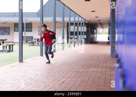 In der Schule, draußen, läuft ein junger männlicher Student mit einem roten Rucksack mit Kopierraum Stockfoto