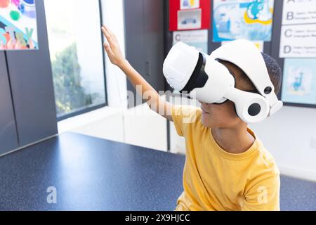 In einer Schule erforscht ein birassischer Junge die virtuelle Realität mithilfe eines Headsets im Klassenzimmer Stockfoto