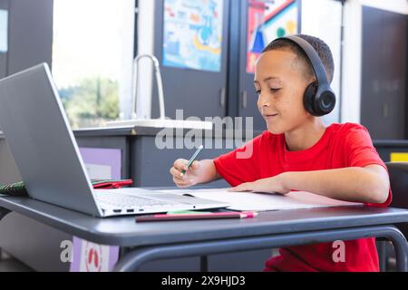 Biracial Boy studiert intensiv in einer Schulklasse mit einem Laptop, mit Kopierraum Stockfoto