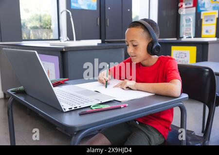 Biracial Boy studiert intensiv in einer Schulklasse mit einem Laptop, mit Kopierraum Stockfoto