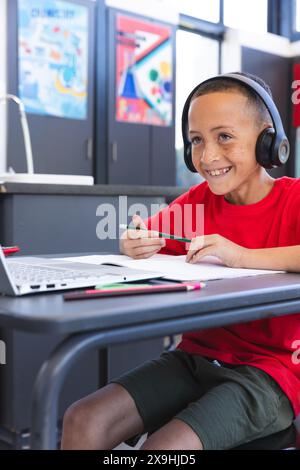 Biracial Boy studiert in der Schule mit einem Laptop, mit Kopierraum. Er konzentriert sich auf seine Arbeit mit Kopfhörern. Stockfoto