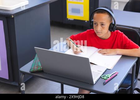 Biracial Boy studiert intensiv in einer Schulklasse mit einem Laptop, mit Kopierraum Stockfoto