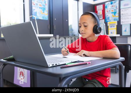 Biracial Boy studiert intensiv in einer Schulklasse mit einem Laptop, mit Kopierraum Stockfoto