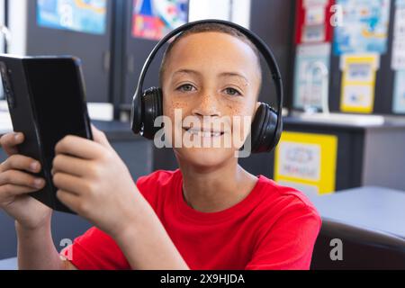 Biracial Boy genießt Musik auf seinem Tablet im Klassenzimmer mit einem Tablet Stockfoto