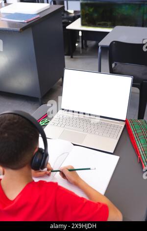 Biracial Boy studiert in einem Schulklassenzimmer mit einem Laptop, mit Kopierraum Stockfoto