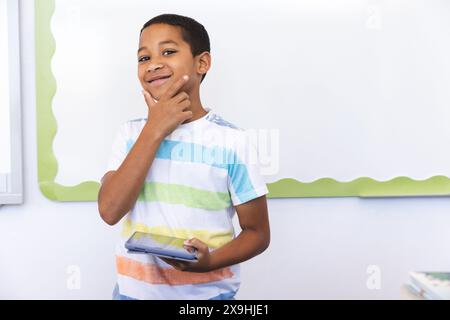 Ein birassischer Junge hält in der Schule ein Tablet in einem Klassenzimmer Stockfoto