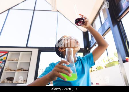 Biracial Boy untersucht ein Reagenzglas in einem hellen Klassenzimmer mit Kopierraum Stockfoto