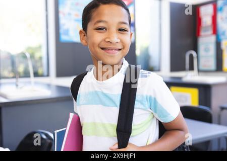 Ein birassischer Junge lächelt hell in einem Klassenzimmer in der Schule Stockfoto