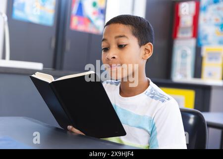 Ein birassischer Junge liest ein Buch in einem Klassenzimmer in der Schule Stockfoto