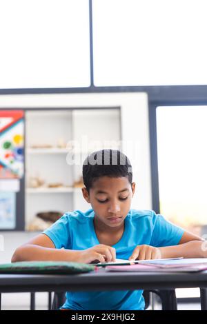 Biracial Boy konzentriert sich auf seine Schularbeit in einem Klassenzimmer in der Schule Stockfoto