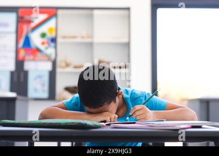 Biracial Boy konzentrierte sich auf das Schreiben in einem Klassenzimmer in der Schule Stockfoto