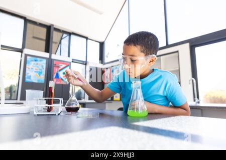 Ein birassischer Junge, der in der Schule an einem wissenschaftlichen Experiment teilgenommen hat, in einem Klassenzimmer mit Kopierraum Stockfoto