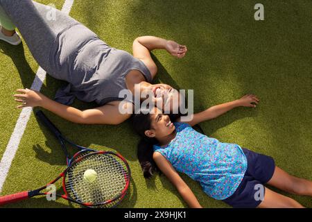 Im Freien liegend Mutter und Tochter mit Tennisschlägern auf Gras, lächelnd Stockfoto