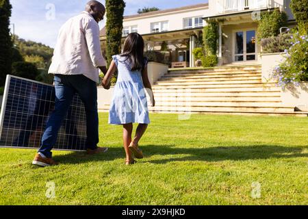 Im Freien, vielfältiger Vater und Tochter, die in Richtung eines modernen Hauses laufen Stockfoto