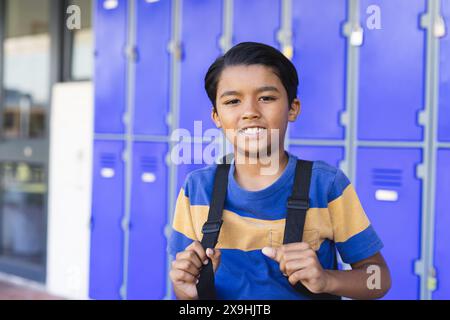 Birassischer Junge mit Rucksack steht vor blauen Schließfächern in der Schule Stockfoto