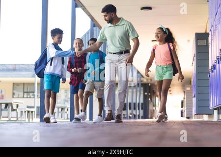 In der Schule läuft ein asiatischer Lehrer mit drei rassistischen Jungen und Mädchen Stockfoto