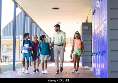 Junger asiatischer Lehrer läuft mit einer Gruppe verschiedener Kinder in einem Schulflur Stockfoto