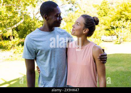 Ein vielfältiges junges Paar, das draußen im sonnigen Park steht Stockfoto