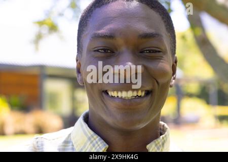Ein junger Afroamerikaner, der draußen lächelt und ein kariertes Hemd trägt. Mit kurzen schwarzen Haaren und klarer Haut, Sonnenschein und frische Luft, u Stockfoto