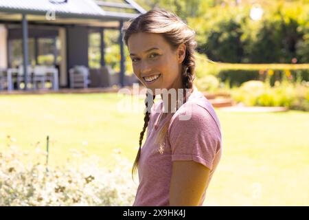 Eine weiße junge Frau, die ein rosa Hemd trägt und draußen lächelt Stockfoto