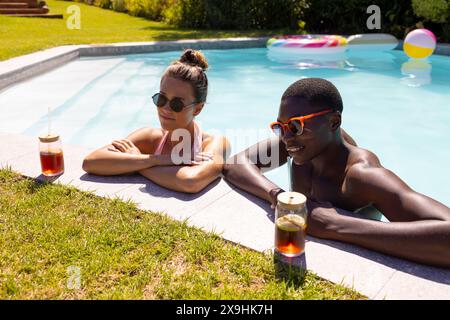 Ein vielfältiges junges Paar, das sich draußen am Pool erholt Stockfoto