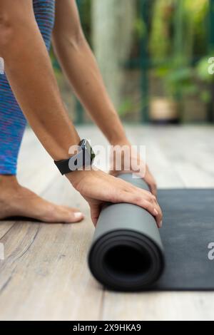 Das Glashaus-Studio zeigt die Pazifikinsel-Frau, die Yoga-Matte auf Holzboden aufrollte Stockfoto