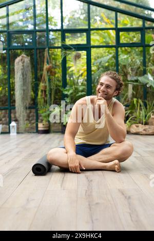 Kaukasischer Mann in gelbem Oberteil, blaue Shorts lächelt beim Glass House Studio Yoga Kurs Stockfoto