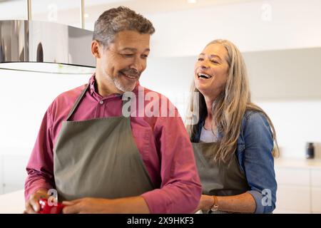 Zu Hause lächelt und lacht ein vielseitiges Seniorenpaar in der Küche Stockfoto